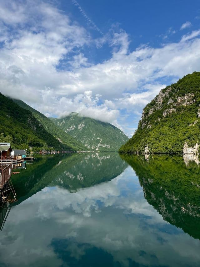 Des montagnes abruptes et verdoyantes et un ciel partiellement nuageux se reflètent dans les eaux calmes d'un lac.