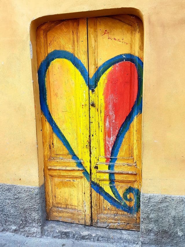 A large, colorful heart with a blue outline is painted across a weathered yellow wooden door.