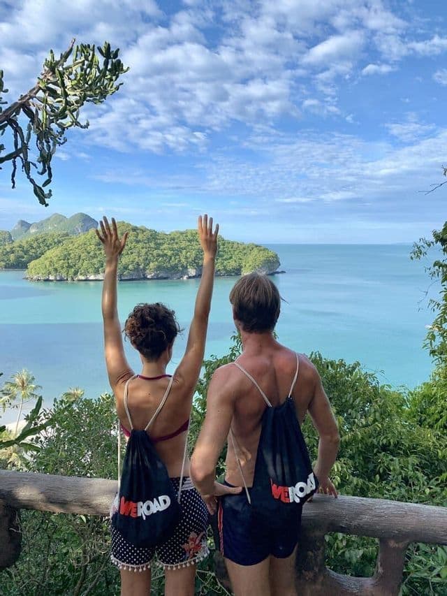 Un uomo e una donna, durante un viaggio di gruppo WeRoad, ammirano una baia tropicale con isole verdi; la donna alza le braccia al cielo.