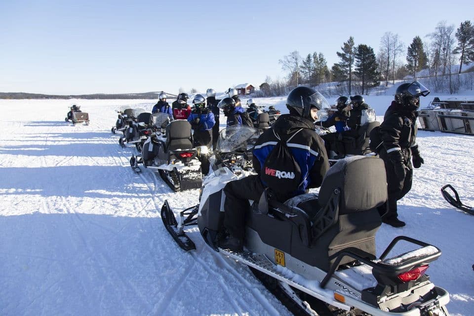 Un viaje en grupo de WeRoad con cascos y equipo de invierno, preparándose para conducir motos de nieve alineadas en un paisaje nevado.