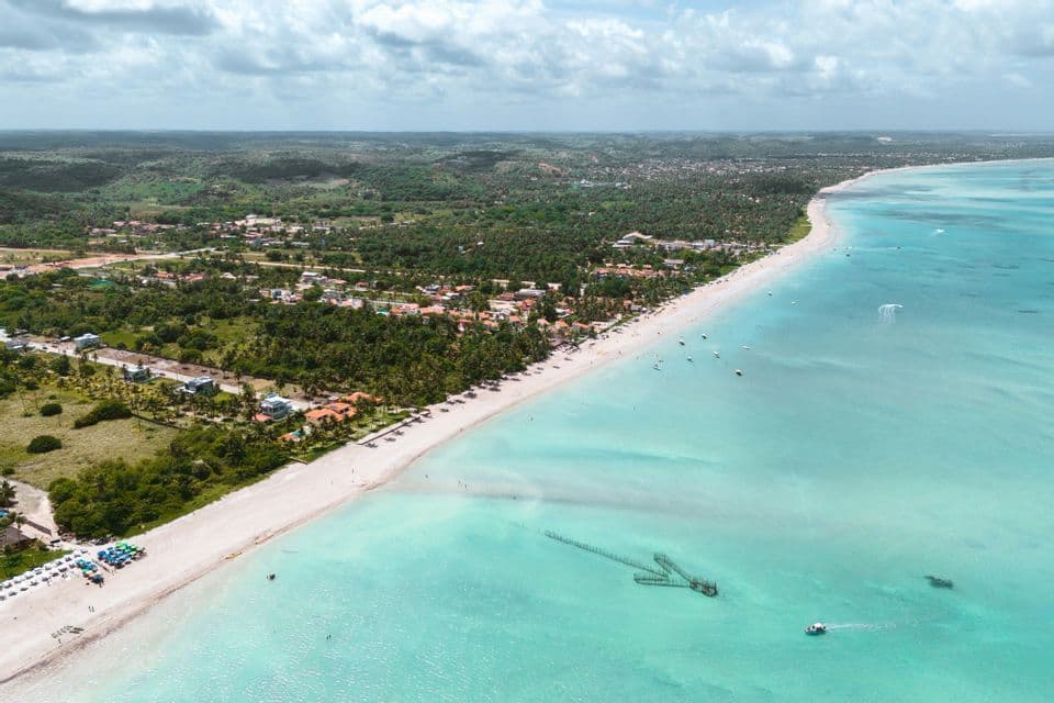 Una vista aerea di una costa tropicale, con una spiaggia di sabbia bianca che separa un paesaggio verde lussureggiante da acque limpide e turchesi.