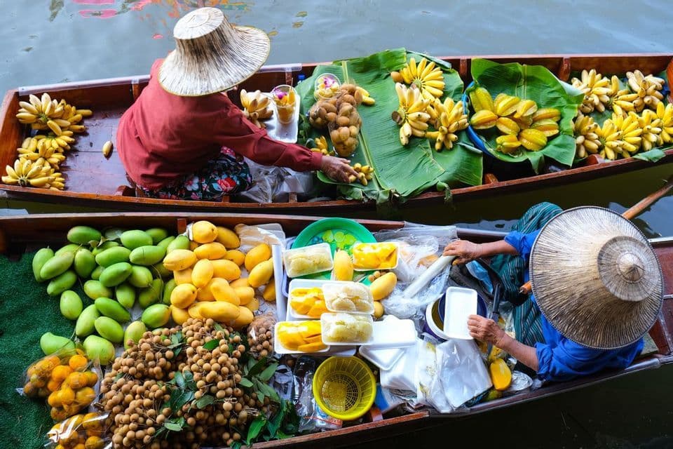 Una vista dall'alto di due venditori con cappelli tradizionali che vendono frutta tropicale fresca dalle loro barche di legno in un mercato galleggiante.