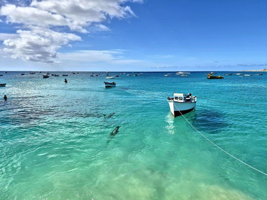 Una barca bianca è ancorata in acqua cristallina color turchese, con molte altre barche visibili in lontananza sotto un cielo blu.