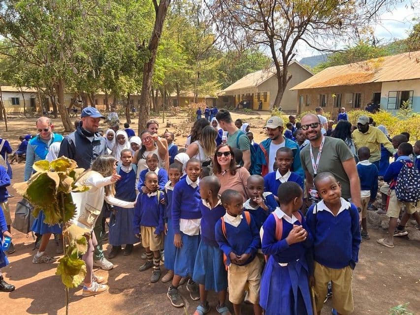 Un gruppo WeRoad in viaggio si mette in posa per una foto con un folto gruppo di scolari in divisa blu in un cortile della scuola.