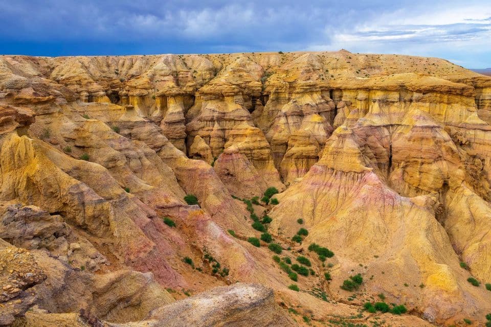 Paysage de badlands coloré aux formations rocheuses érodées jaunes et roses sous un ciel sombre et orageux.