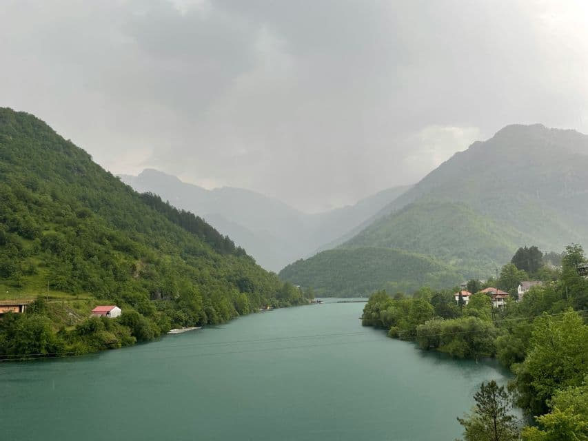 Une rivière turquoise serpente à travers une vallée entre des montagnes verdoyantes et luxuriantes sous un ciel nuageux.