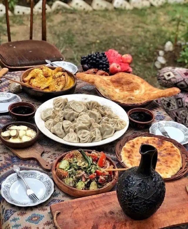 Eine Auswahl traditioneller Gerichte, darunter Knödel, Fladenbrot und Salat, auf einem rustikalen Tisch für ein Festmahl im Freien.