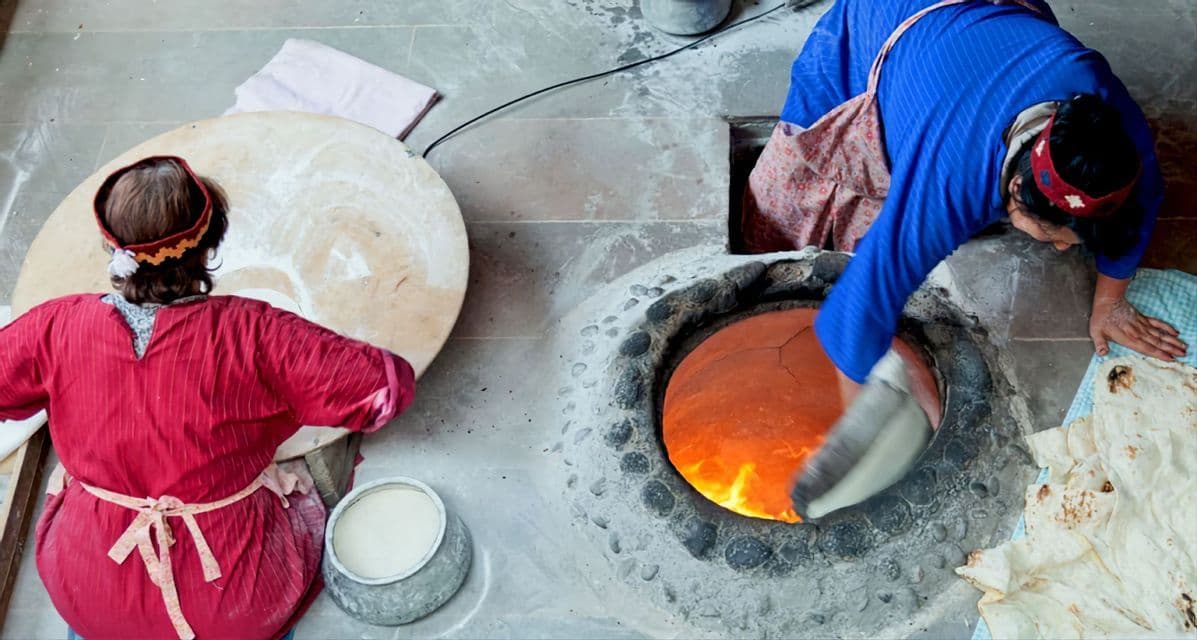 Draufsicht auf zwei Frauen beim Fladenbrotbacken, wobei eine den Teig in einen traditionellen, feurigen Tandoor-Ofen legt.