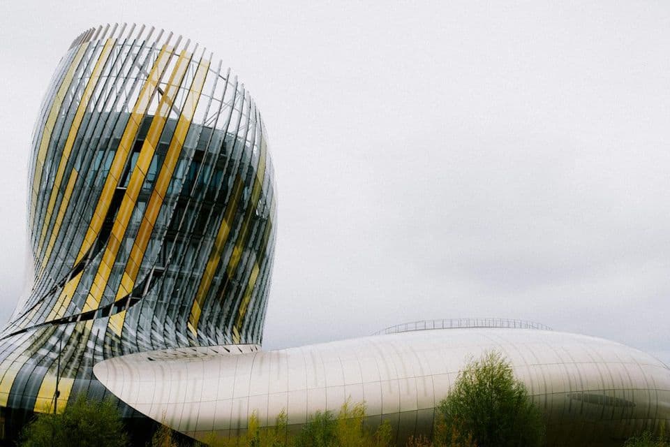 Un edificio moderno e curvo con pannelli a spirale gialli e di vetro accanto a una struttura bassa e bianca sotto un cielo coperto.