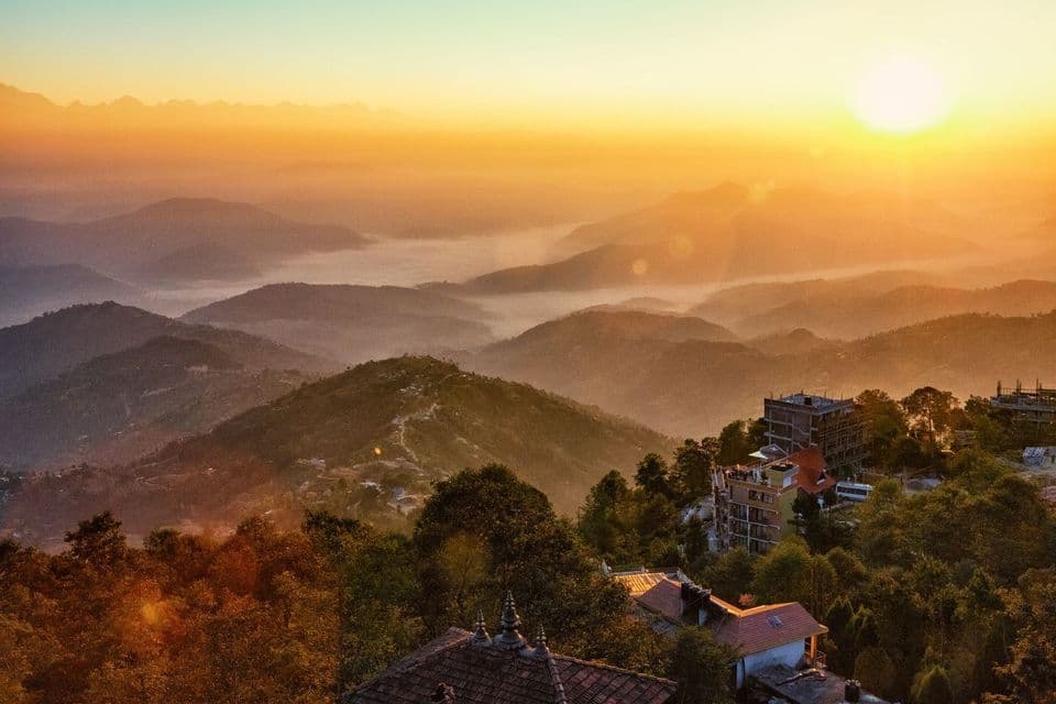 Il sole sorge tra le montagne, proiettando un bagliore dorato su valli nebbiose ed edifici in primo piano.