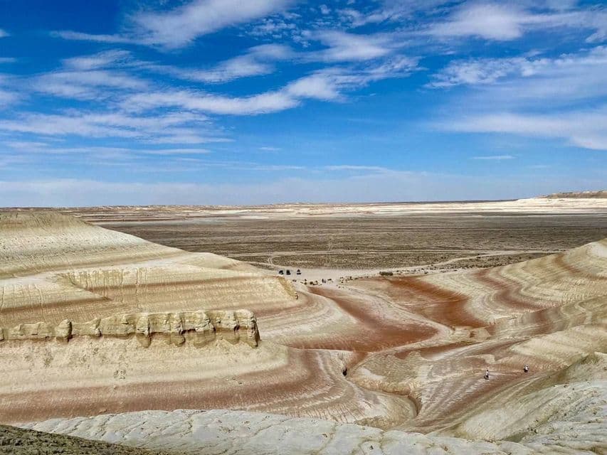 Un viaggio di gruppo WeRoad esplora un vasto canyon con formazioni rocciose colorate e stratificate sotto un cielo azzurro brillante.