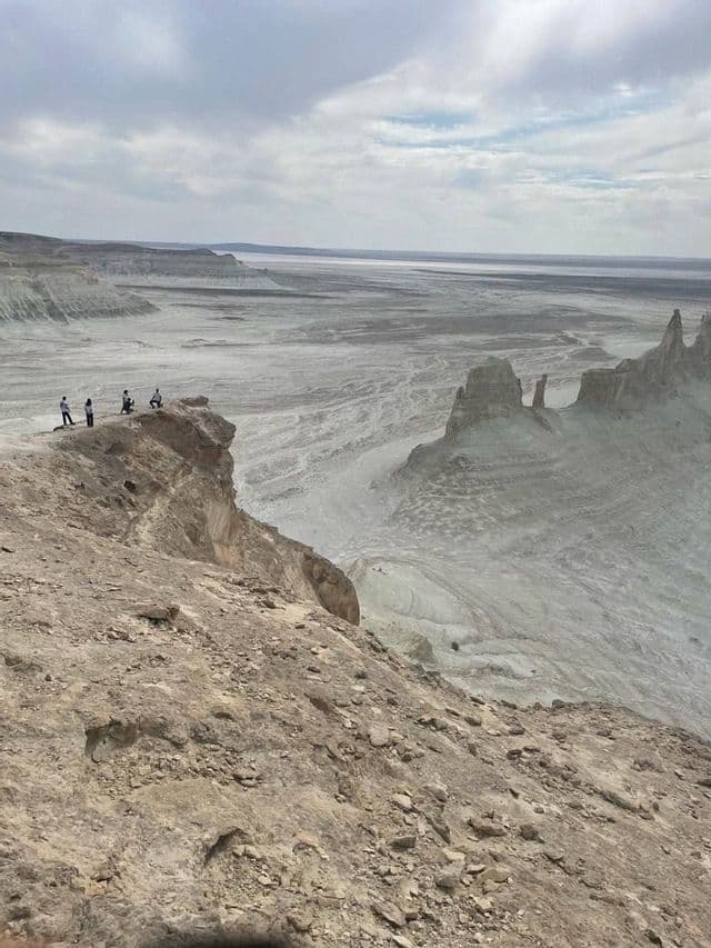 Un gruppo WeRoad di quattro persone in piedi sul bordo di una scogliera rocciosa, con vista su una vasta valle arida sotto un cielo nuvoloso.