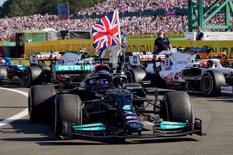 A black Formula 1 car on a racetrack with a person holding a British flag and a crowd of spectators in the background.