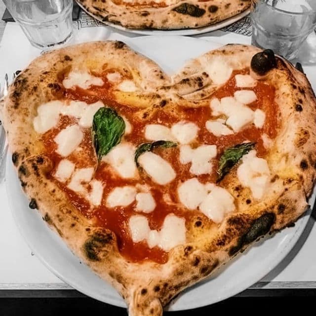 Eine herzförmige neapolitanische Pizza mit Mozzarella und Basilikum, serviert auf einem weißen Teller.
