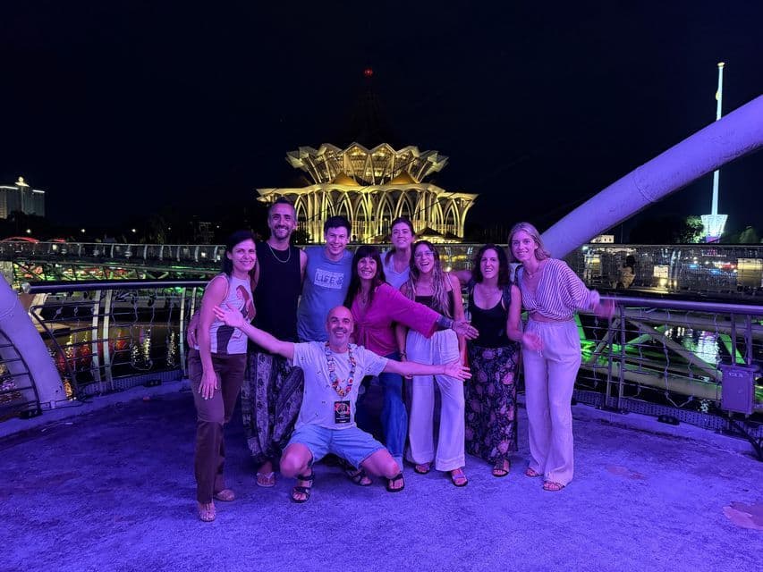 Un viaje en grupo de WeRoad posando para una foto en un puente moderno por la noche, con un gran edificio iluminado de fondo.