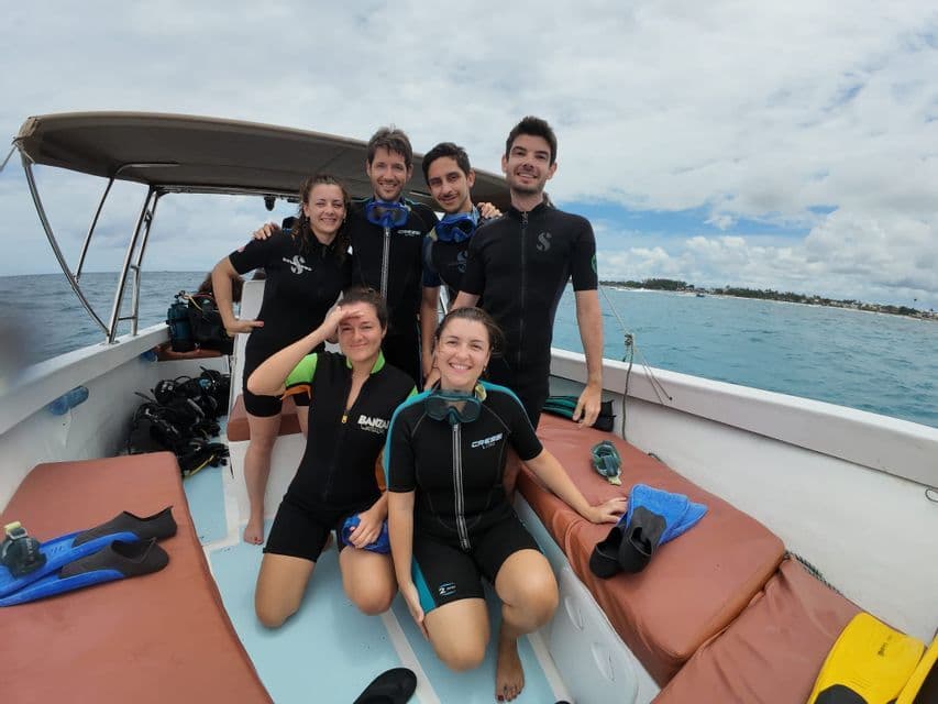 Un voyage de groupe WeRoad en combinaisons de plongée posant pour une photo sur un bateau avant une plongée en pleine mer.