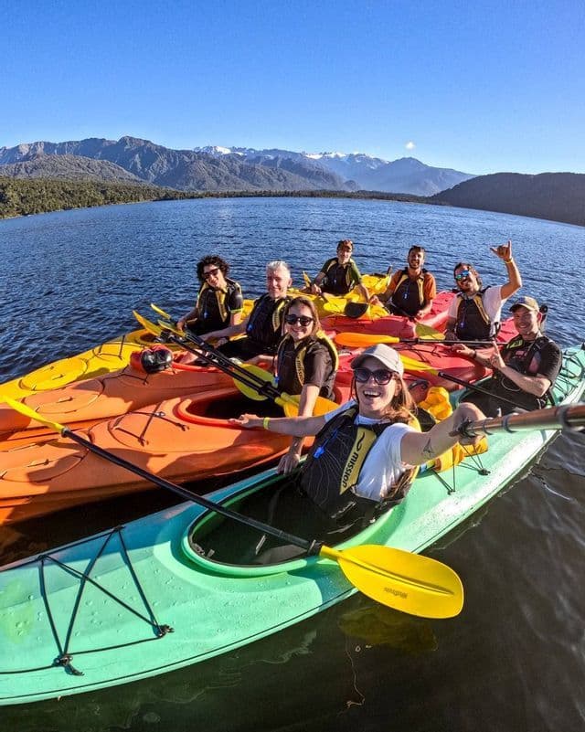 Eine WeRoad Gruppenreise macht ein Selfie beim Kajakfahren auf einem ruhigen See mit Bergen im Hintergrund.