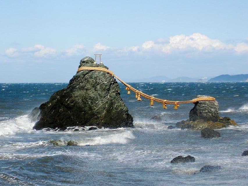 Due grandi scogli in un mare mosso sono uniti da una spessa corda, con un piccolo portale torii sulla cima dello scoglio più grande.