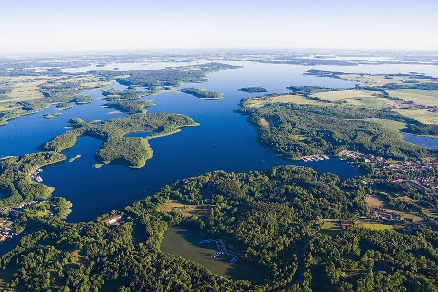 Vue aérienne d'une vaste région des lacs, avec des îles verdoyantes et boisées parsemant l'eau d'un bleu profond sous un ciel dégagé.