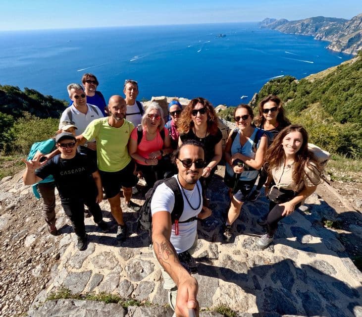 Un grupo de WeRoad se toma una selfie haciendo senderismo por un sendero junto al acantilado con vistas al inmenso mar azul y la costa.