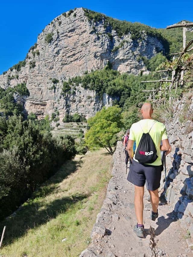 Un viaje en grupo de WeRoad de senderismo por un sendero rocoso a lo largo de una empinada ladera verde en un día soleado.