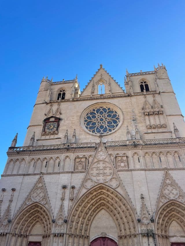 Une vue en contre-plongée de la façade en pierre ornée d'une cathédrale gothique, présentant une grande rosace et des flèches sur un ciel bleu clair.