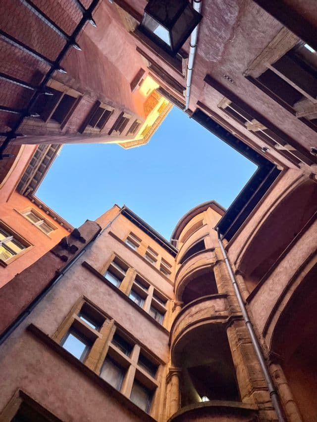 Vue en contre-plongée depuis une cour, vers des bâtiments historiques encadrant un coin de ciel bleu clair.