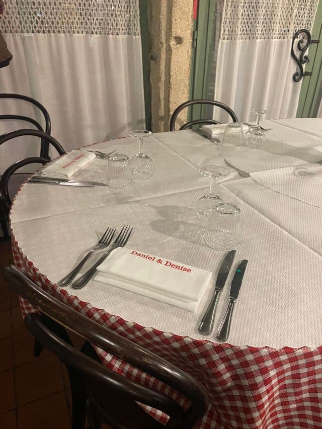 Une table dressée dans un restaurant avec une nappe à carreaux rouges et blancs, des couverts, des verres et une serviette imprimée 'Daniel & Denise'.
