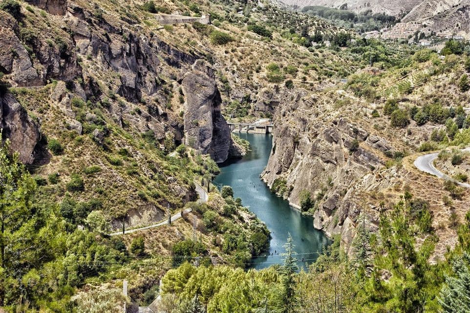 Una vista aérea de un río azul profundo serpenteando por un cañón rocoso, rodeado de laderas verdes y áridas.