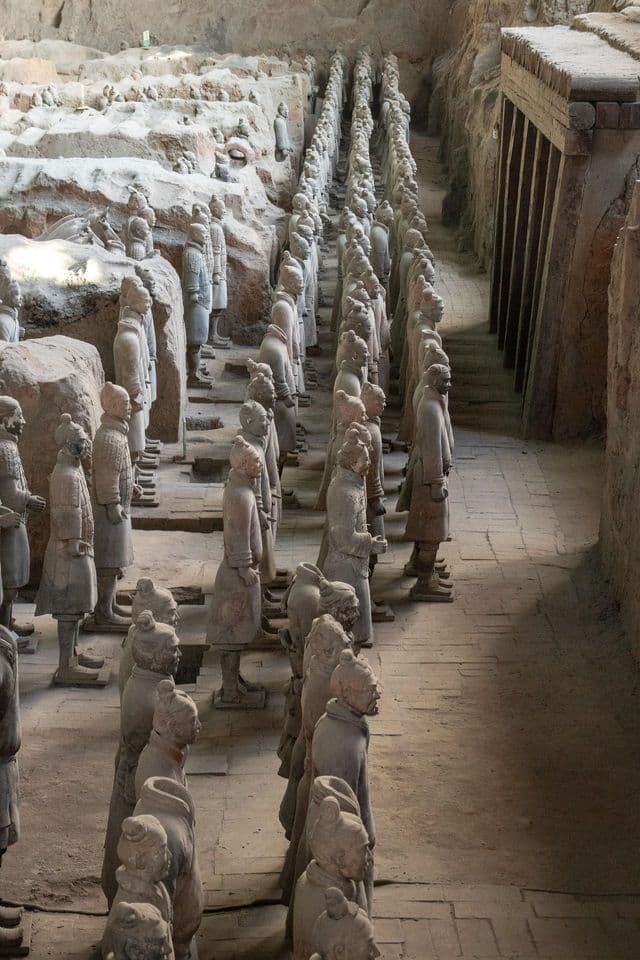 File di statue di guerrieri in terracotta a grandezza naturale, schierate in formazione all'interno di uno scavo archeologico.
