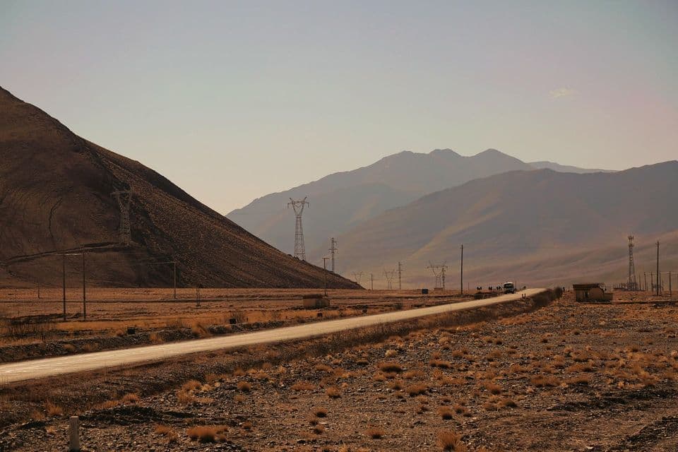Un gruppo WeRoad in viaggio accanto al proprio autobus su una strada che attraversa un paesaggio arido e montuoso con piloni elettrici.