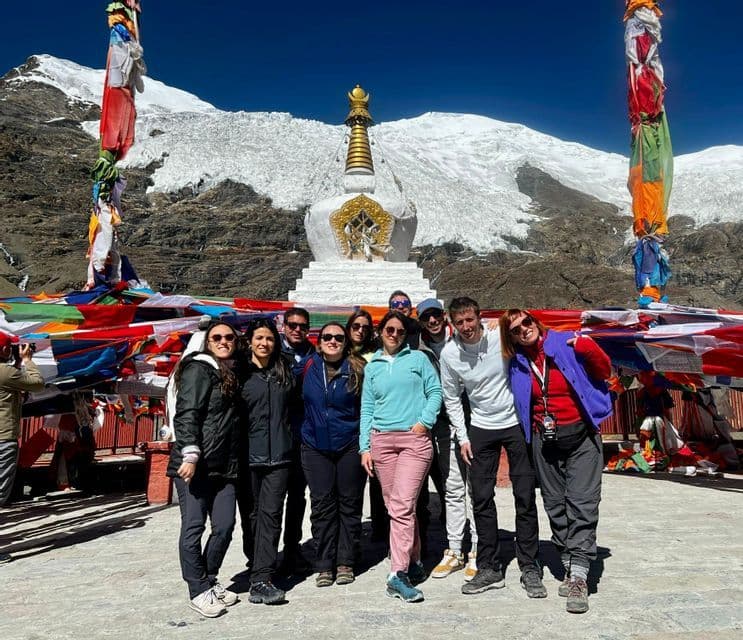 Un viaggio di gruppo WeRoad posa per una foto davanti a uno stupa bianco con un ghiacciaio e montagne innevate sullo sfondo.