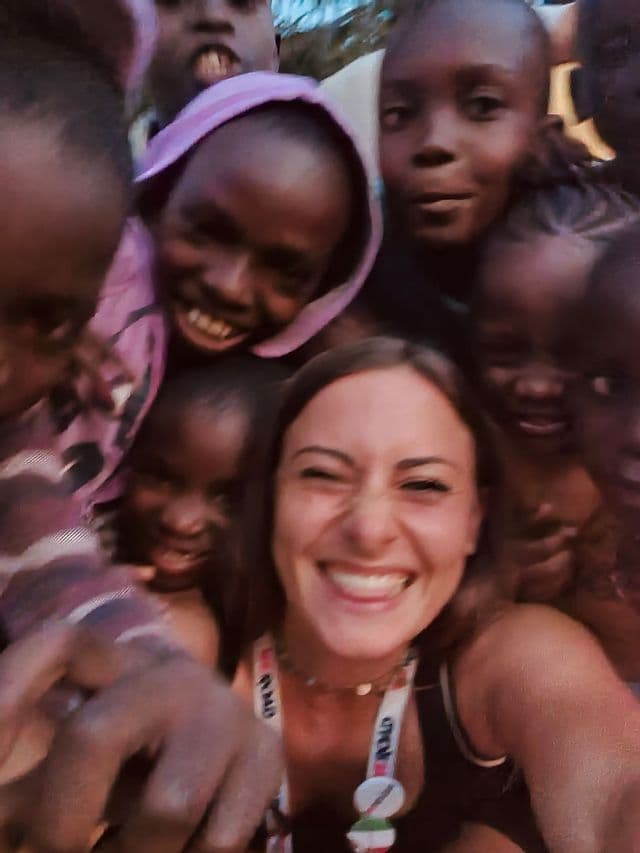 Una donna sorridente in un viaggio di gruppo WeRoad si scatta un selfie ravvicinato con un gruppo di bambini locali che ridono.