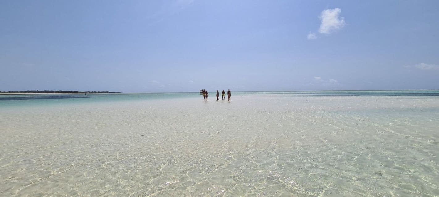 Un gruppo WeRoad in viaggio in acqua bassa e trasparente che si estende fino all'orizzonte sotto un cielo azzurro pallido.