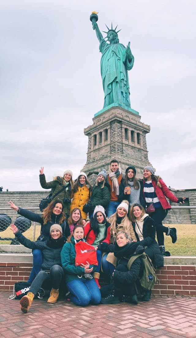 A WeRoad group trip poses for a group photo on brick steps in front of the Statue of Liberty.