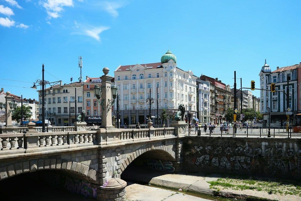 Un puente de piedra ornamentado cruza un canal frente a varios edificios históricos de la ciudad en un día soleado.