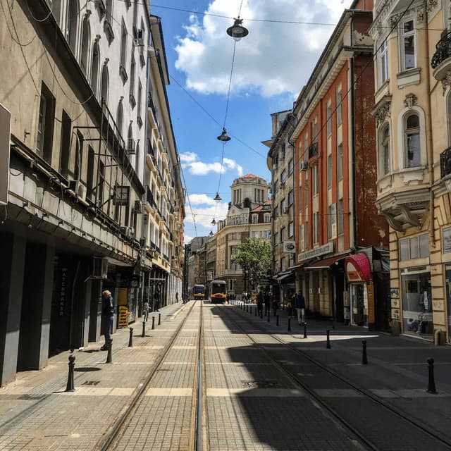 Un tranvía amarillo recorre las vías de una calle de la ciudad flanqueada por edificios de estilo europeo de varios pisos bajo un cielo parcialmente nublado.