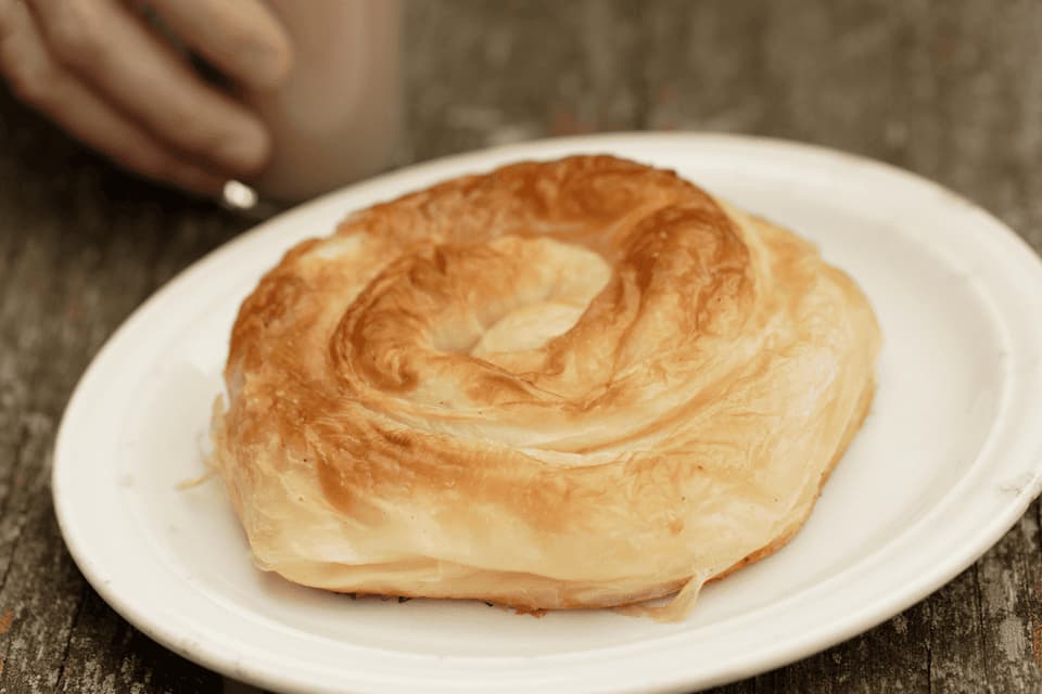 Primer plano de un hojaldre dorado en espiral sobre un plato blanco en una superficie de madera rústica.