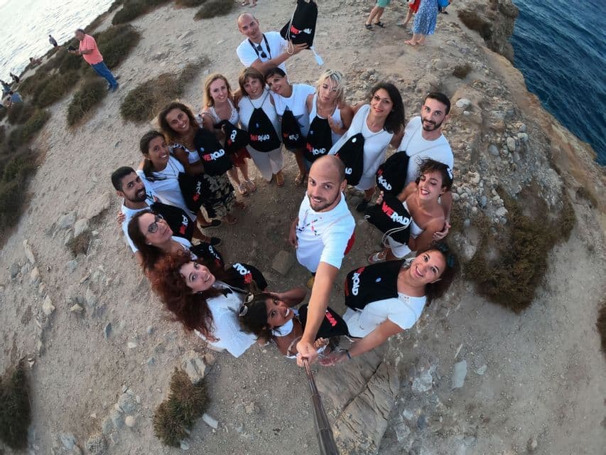 Un selfie dall'alto di un gruppo WeRoad in viaggio che posa in cerchio su una scogliera in riva al mare.