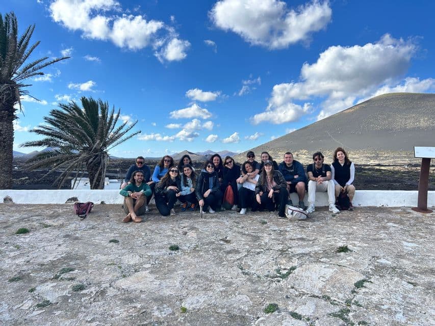 Un gruppo WeRoad in posa per una foto su un punto panoramico in pietra, con una collina vulcanica e palme sullo sfondo.