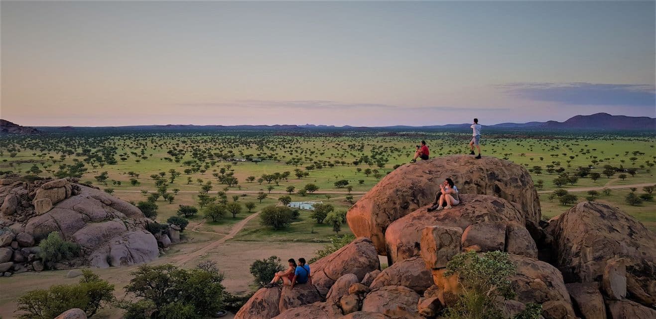 Eine WeRoad-Gruppenreise, bei der man den Sonnenuntergang von großen Felsen aus über einer weiten, von Bäumen übersäten Savanne beobachtet.