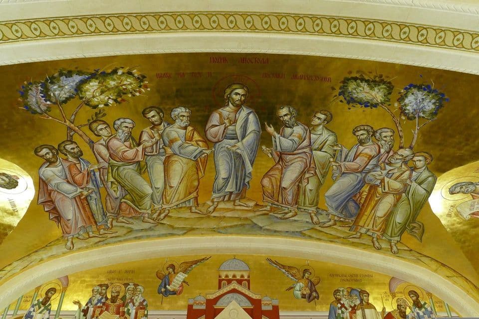 Un fresco bizantino dorado dentro de un arco, representando a Jesucristo con un halo enseñando a sus doce apóstoles reunidos a su alrededor.