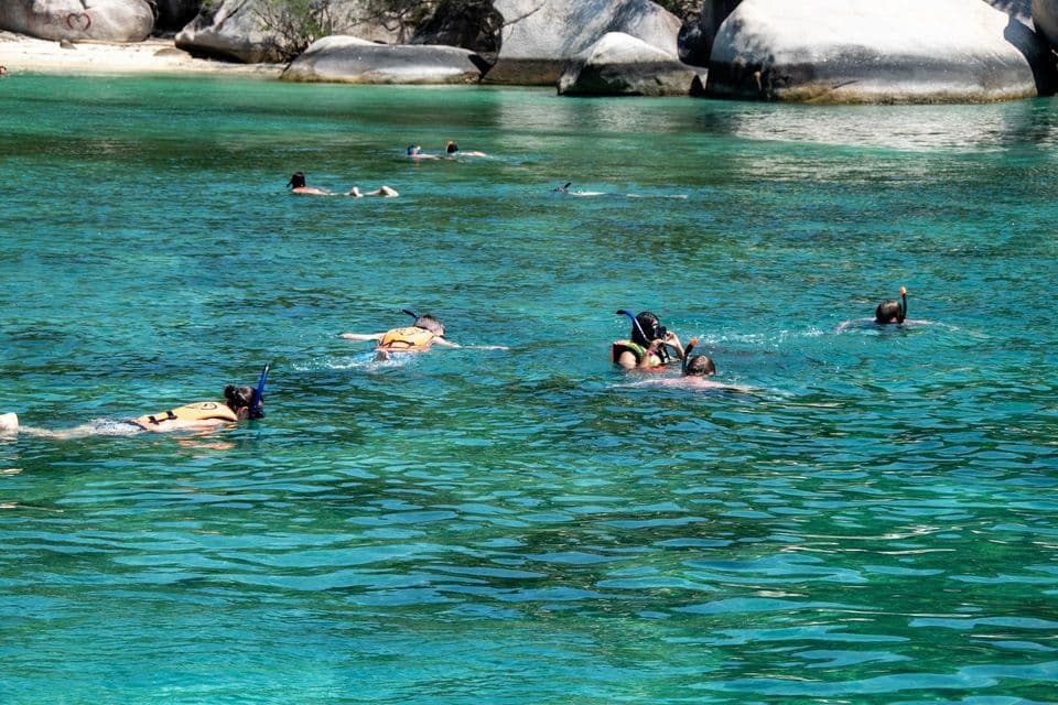 Un viaggio di gruppo WeRoad per fare snorkeling in acque cristalline e turchesi vicino a una costa rocciosa con una spiaggia di sabbia.