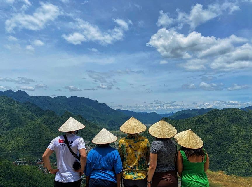 Un viaje en grupo de WeRoad con sombreros cónicos tradicionales contempla un paisaje verde y montañoso bajo un cielo nublado.