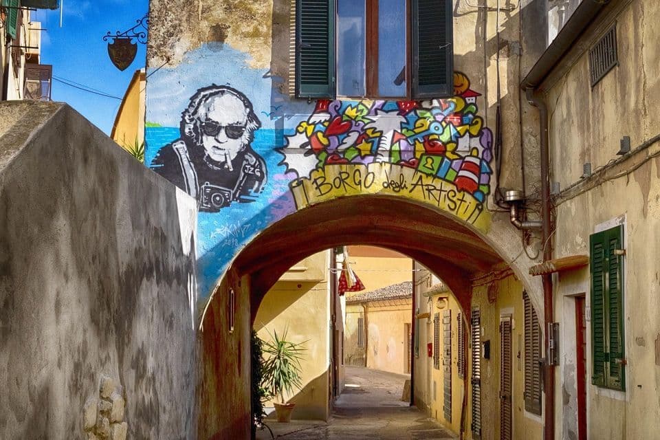 Arte di strada colorata, con la scritta 'Borgo degli Artisti', dipinta su un edificio sopra un arco in un vicolo stretto e soleggiato.