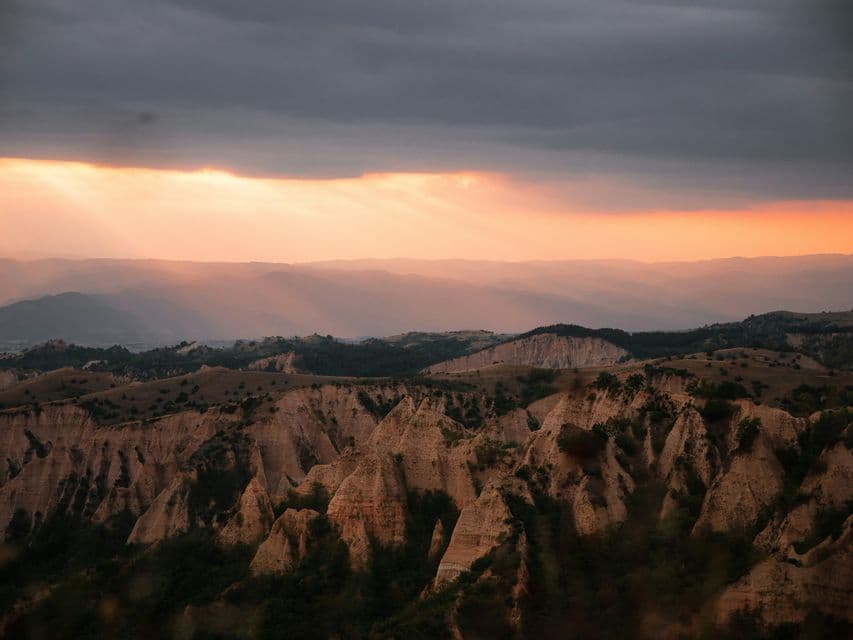 Les rayons du soleil percent les nuages sombres, illuminant un canyon accidenté aux formations rocheuses pointues au coucher du soleil.