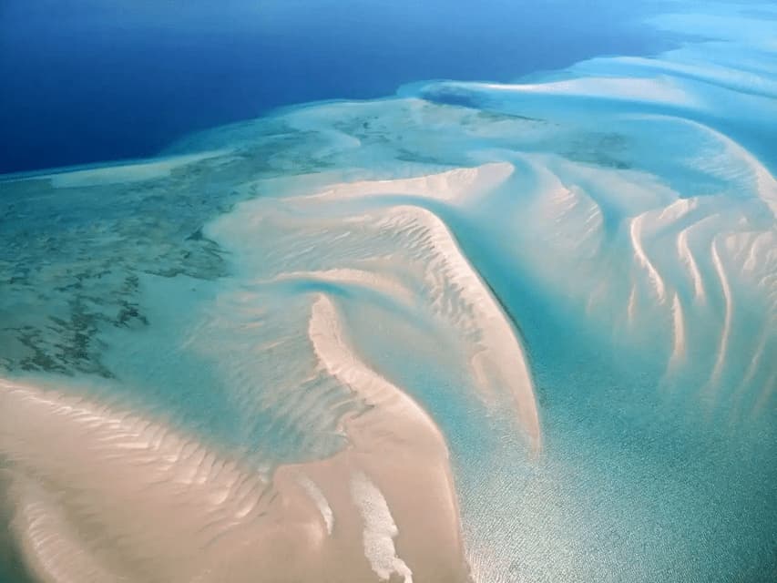 An aerial view of white sandbanks and shallow turquoise water meeting the deep blue ocean.