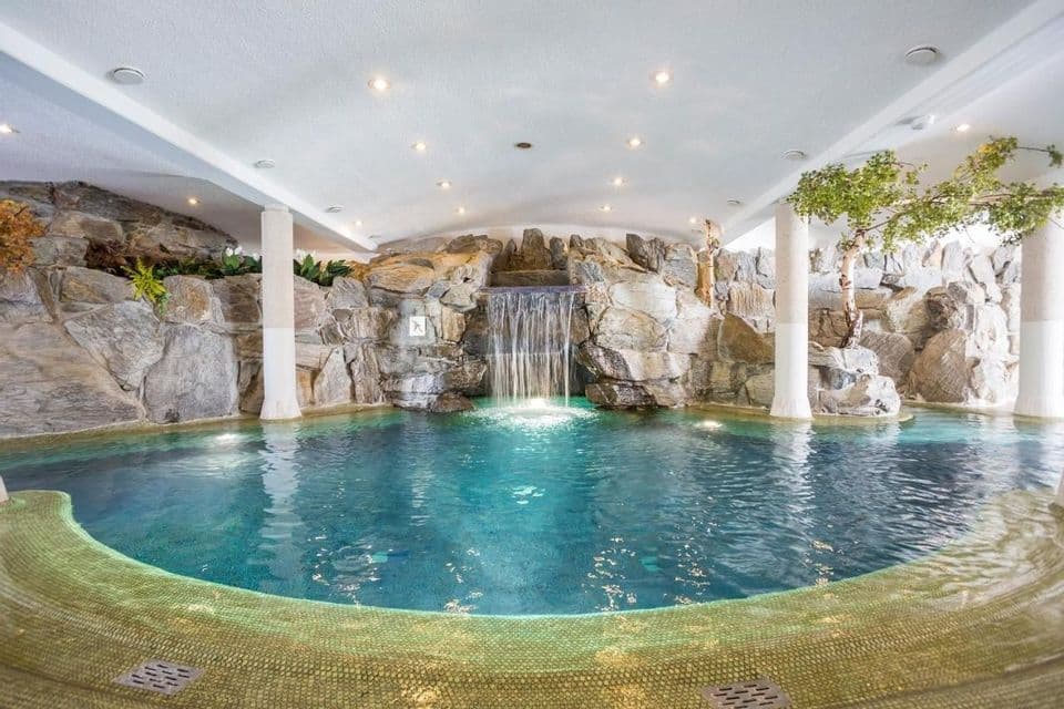 Una piscina interna progettata come una grotta, con una cascata che scorre da una parete rocciosa decorativa nell'acqua turchese.