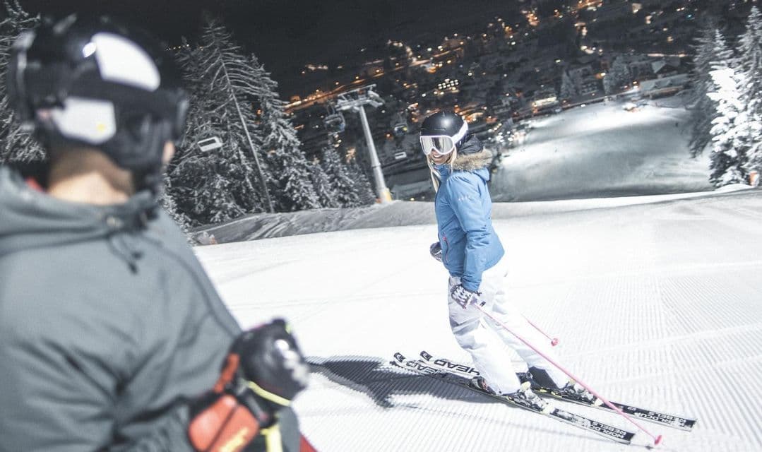 Una donna di un viaggio di gruppo WeRoad sorride alla sua compagna mentre scia di notte su una pista battuta.