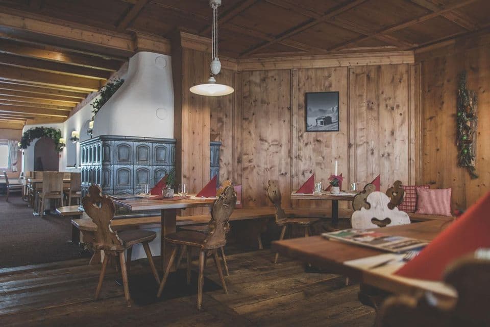 L'interno rustico in legno di un ristorante con tavoli apparecchiati, sedie intagliate e una stufa tradizionale in maiolica.